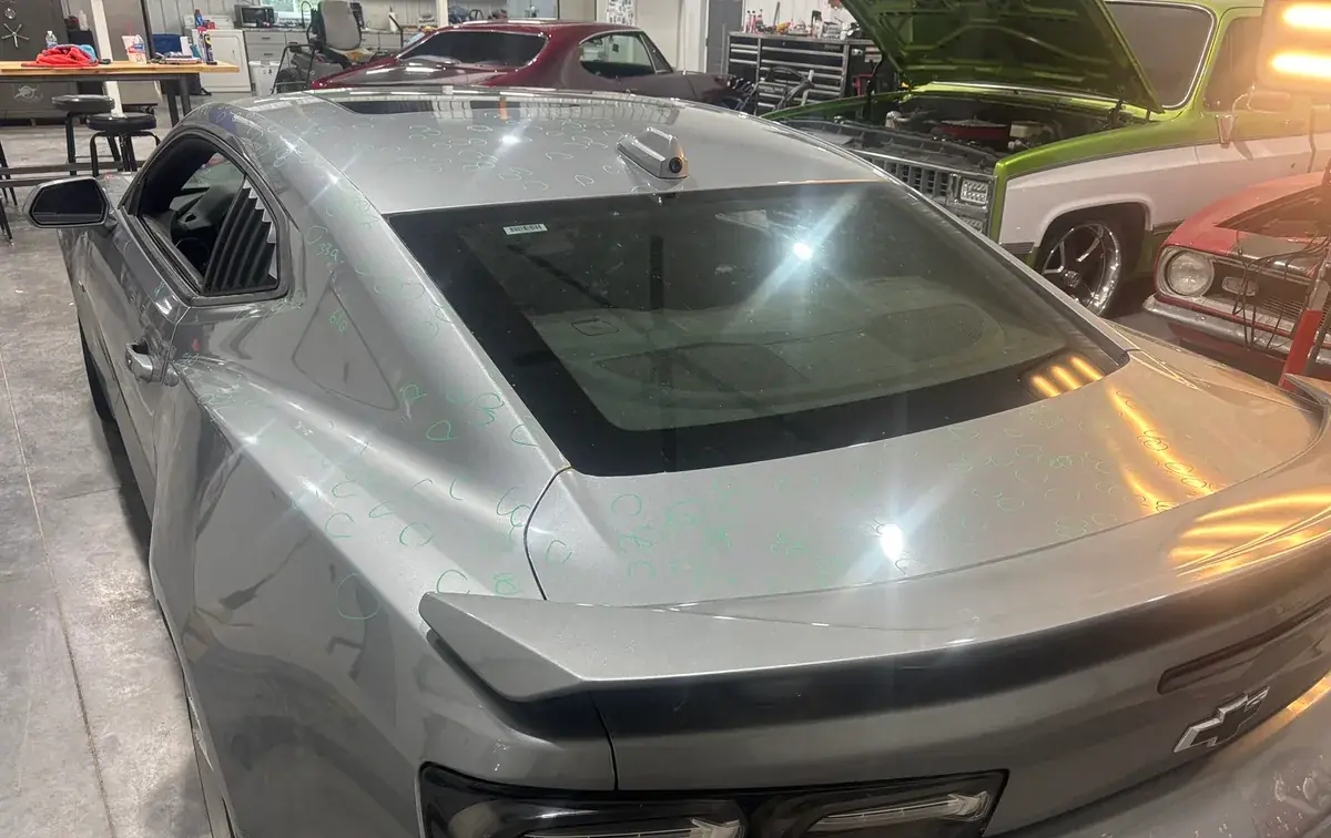 Silver Chevrolet Camaro covered in hail dents marked for repair at the Hail Solutions shop in Olathe, Kansas
