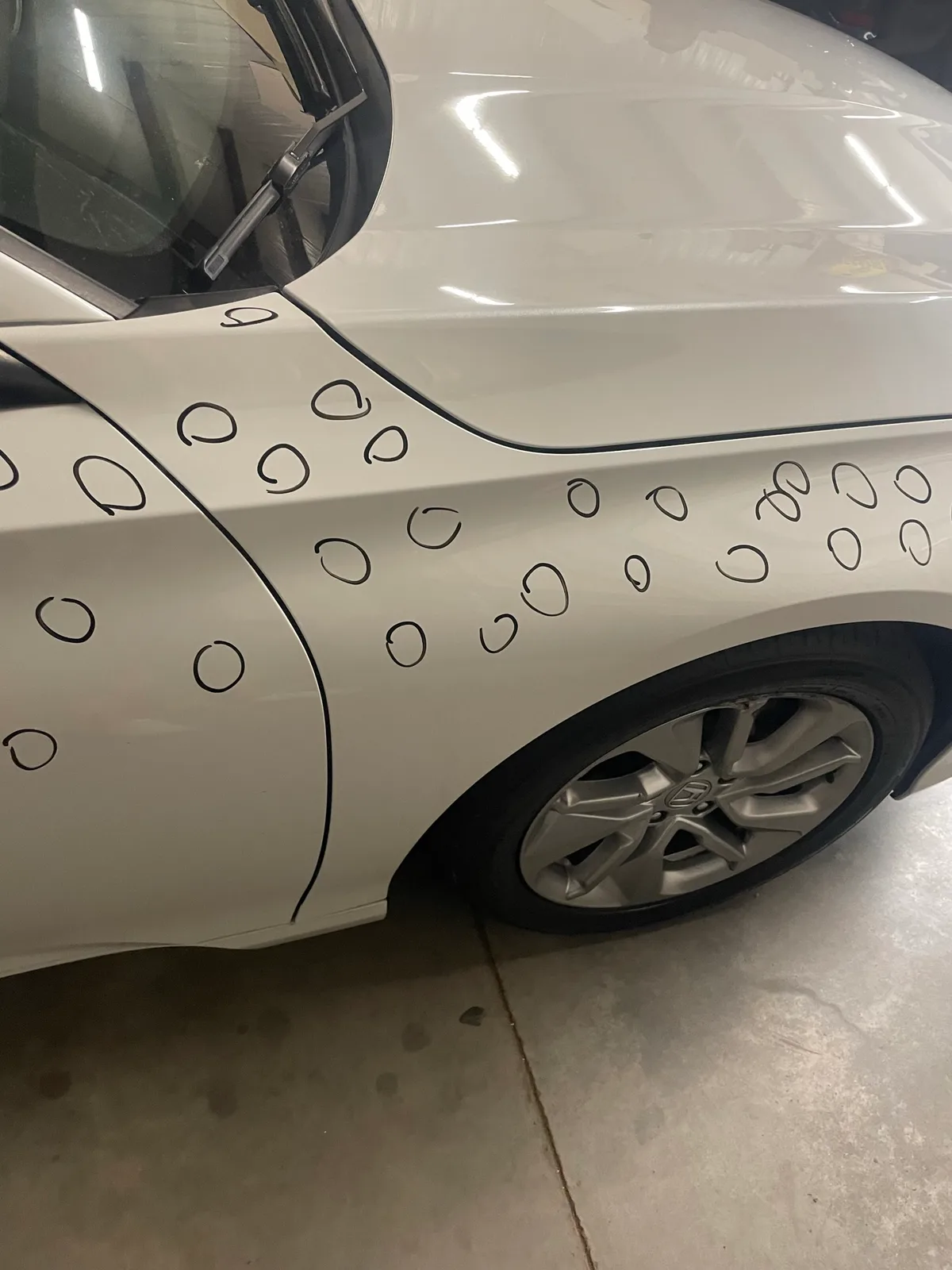 White sedan with individual hail dents circled in marker for damage documentation