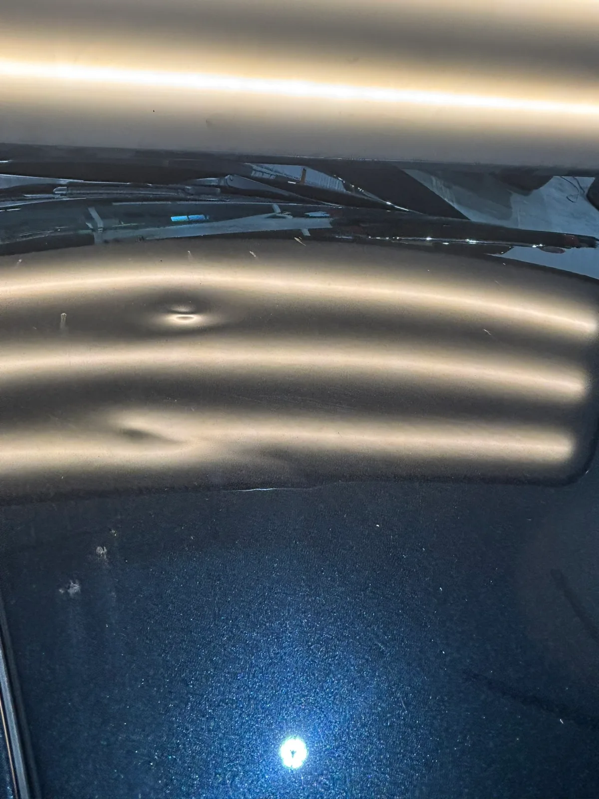 Close-up of hail dents on a vehicle roof with LED stripe reflections