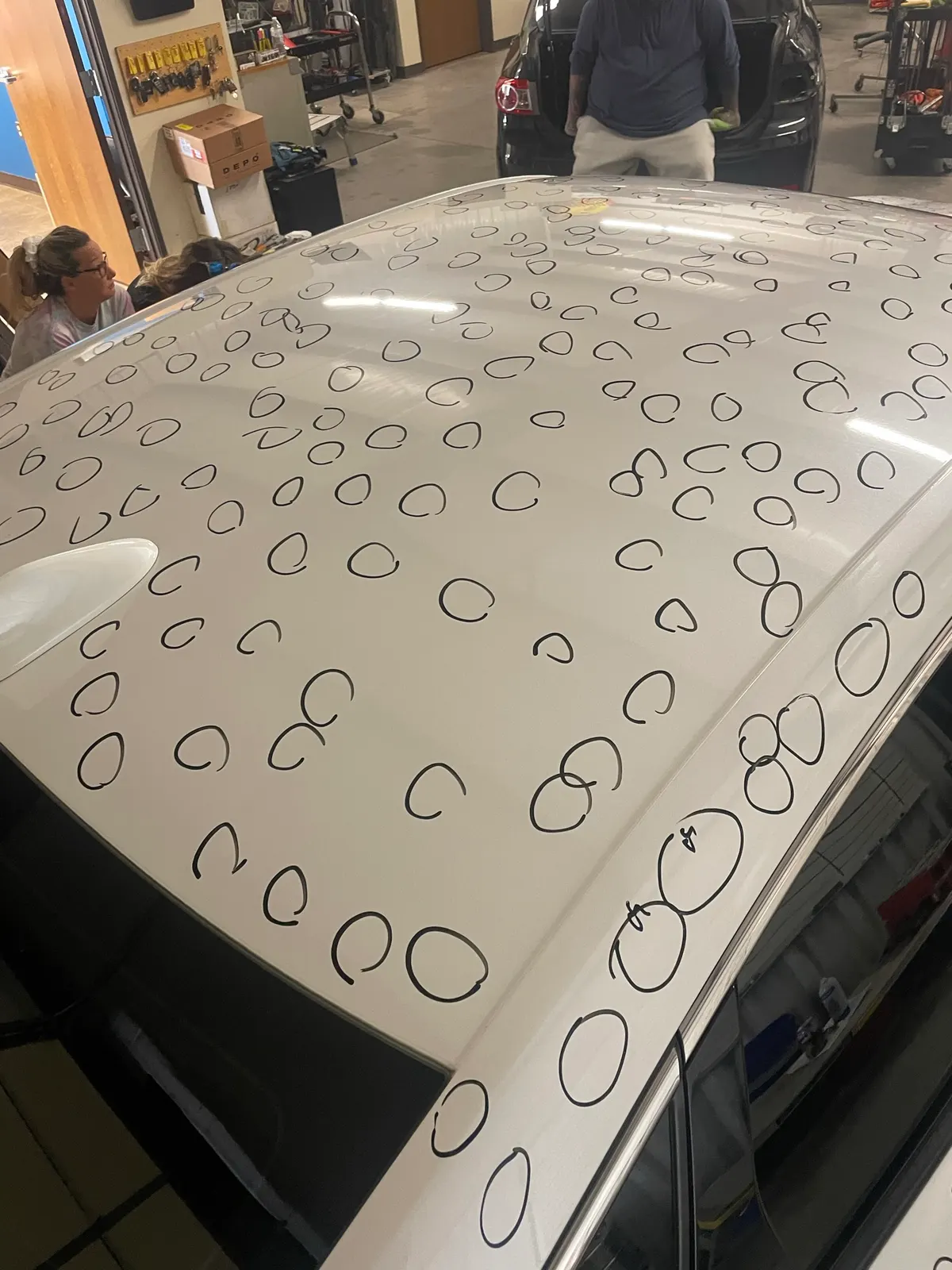 White vehicle roof with over 200 hail dents circled in marker for documentation