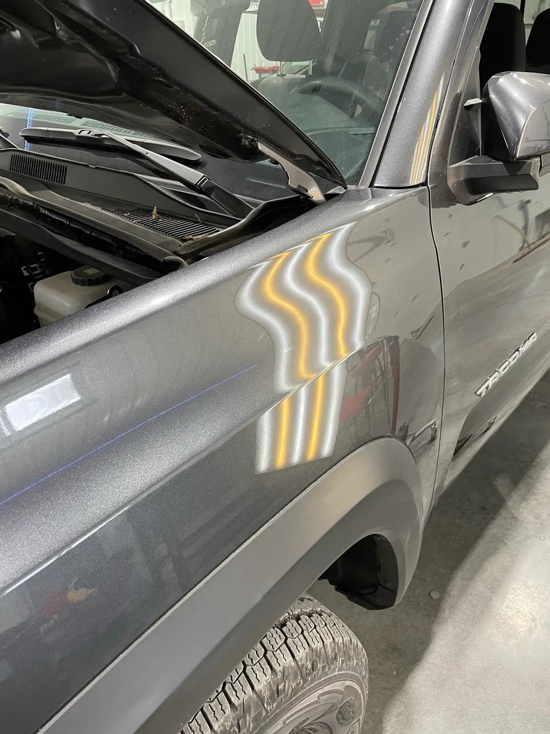 Toyota Tacoma fender panel showing hail dents revealed by LED line-board reflection