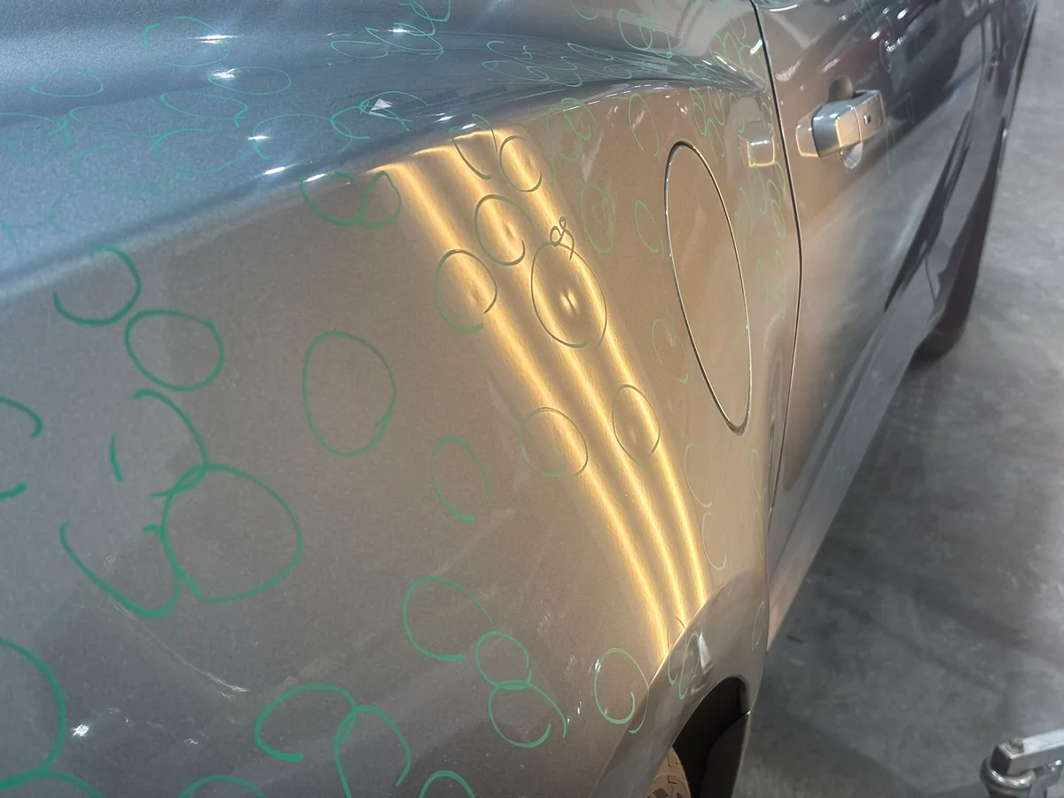 Close-up of severe quarter-size hail dents on a vehicle panel before paintless dent repair at the Olathe shop