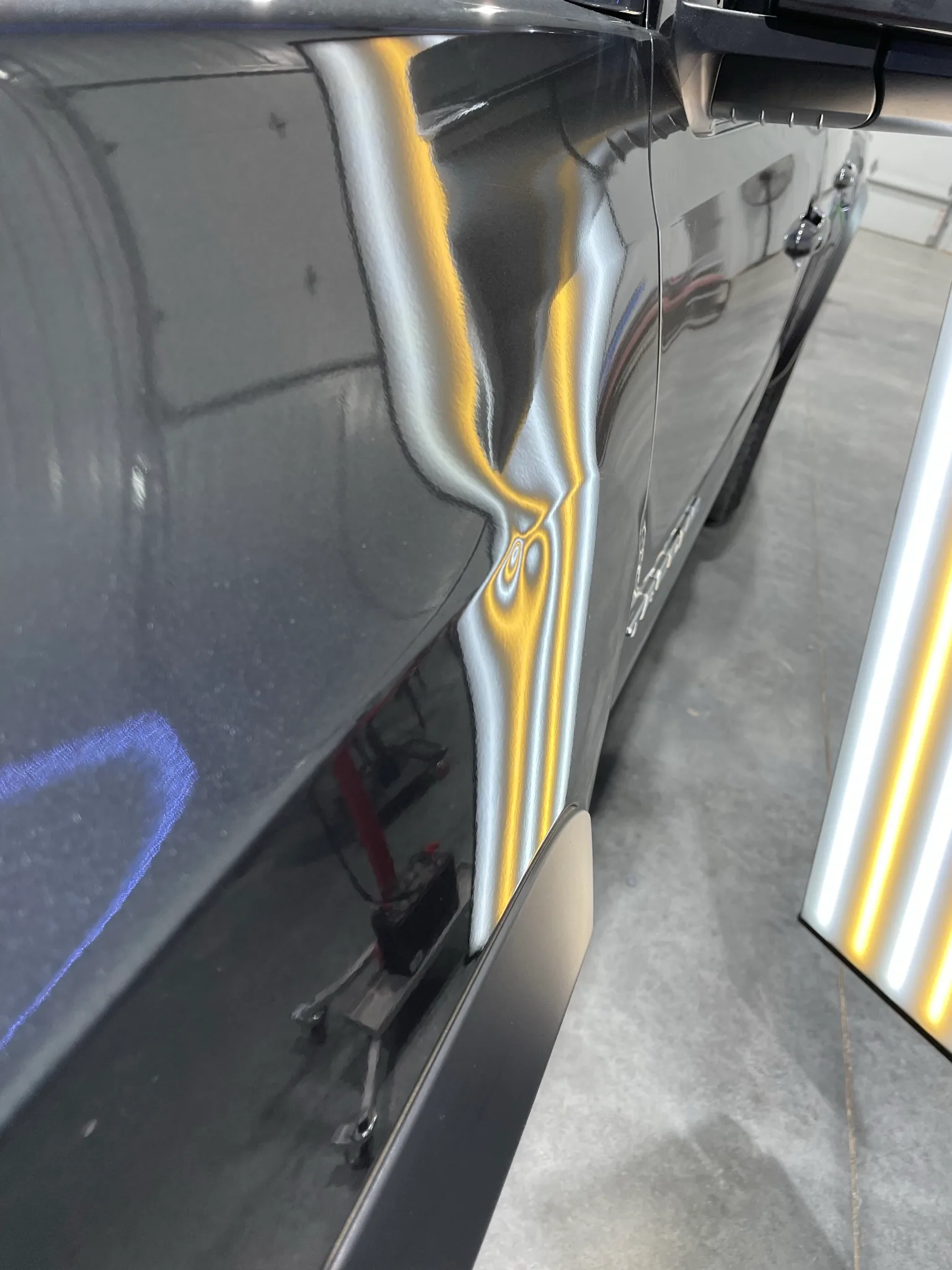 LED line board revealing hail dents on a dark hood during a shop inspection at the Olathe shop